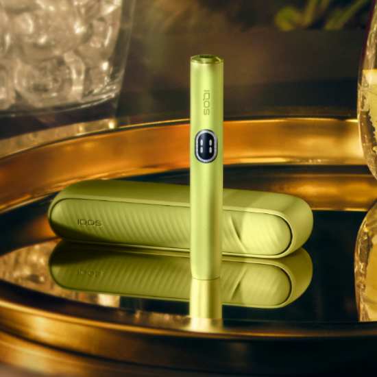 A Leaf Green IQOS ILUMA i device stands on a reflective gold tray.
